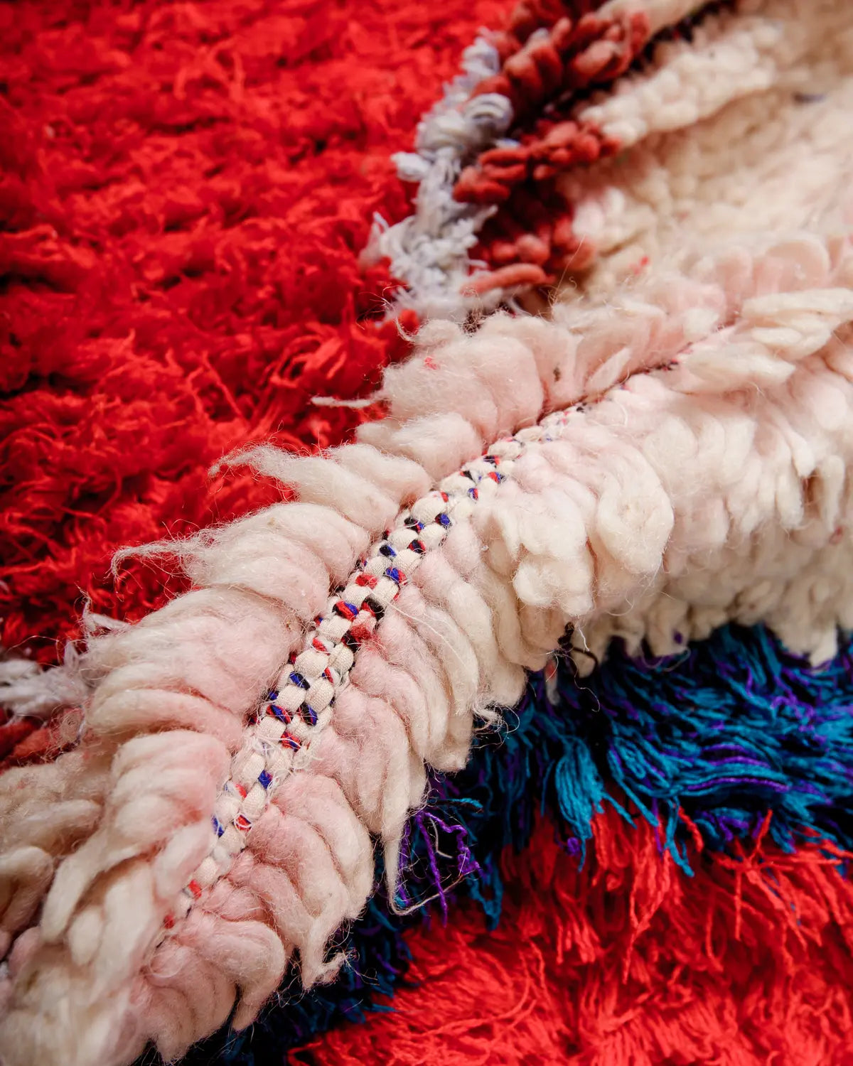 Detail of rug made of wool knotted onto a woven cloth base in reds and pinks.